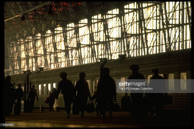 Rail passengers carrying shopping-sized bags walking along platform at Kievsky railway station, framed by waiting train, Moscow (February 19, 1992).jpg